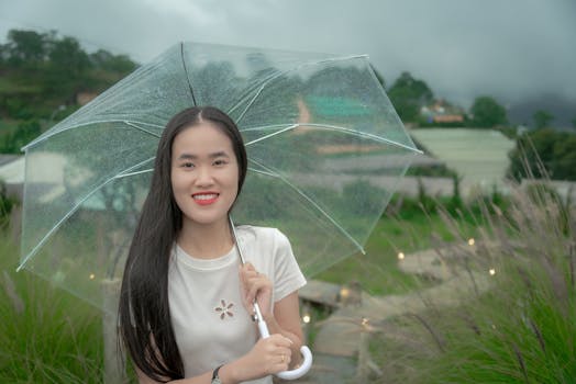Young woman smiling under a clear umbrella in a lush garden setting.