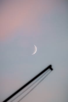 Crescent moon and crane silhouette against a soft evening sky in Hamburg, Germany.