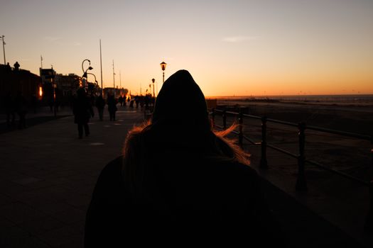 People walking along a promenade at sunset, silhouetted against the sky. Urban and serene.