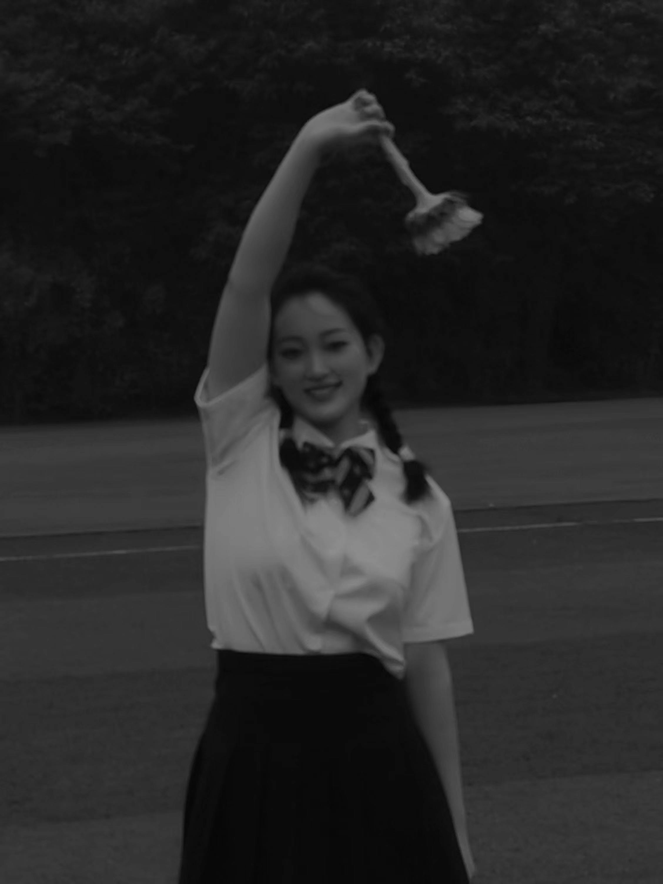 A smiling young woman poses with a flower outdoors, exuding elegance in a black and white setting.