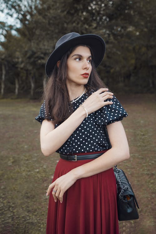 Young Woman in Elegant Clothes and a Hat Standing Outside and Looking Away 
