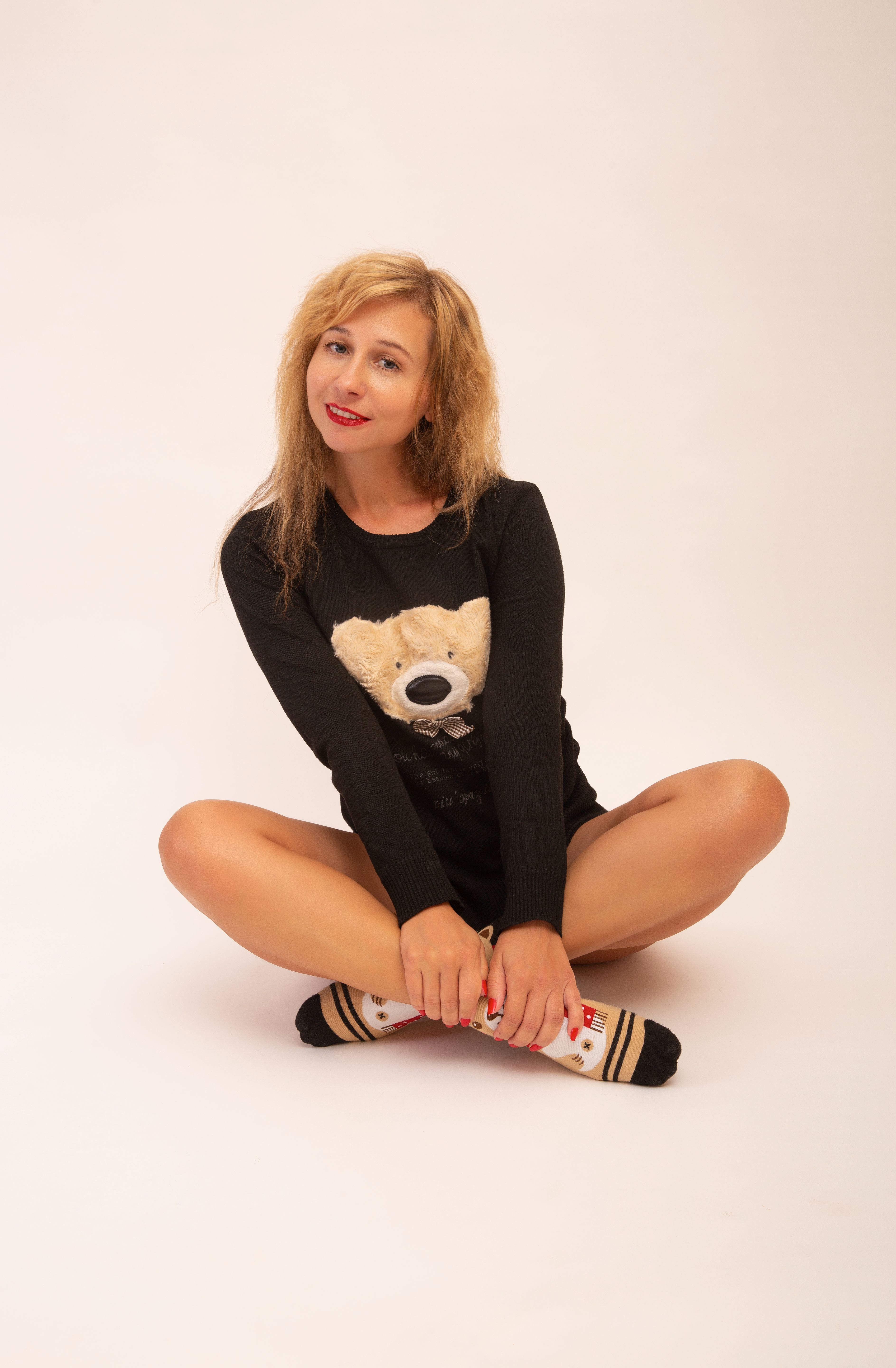 Caucasian woman sitting cross-legged in a cozy teddy bear shirt and striped socks during a studio shoot.