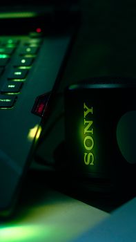 Dynamic close-up of a laptop and speaker with neon green lighting, emphasizing technology and modern design.