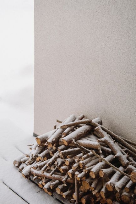 Pile of snow-covered firewood stacked against a wall during winter.