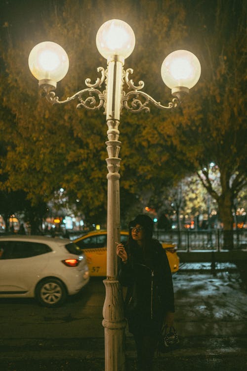 A Woman Standing under a Street Lantern and Smoking 