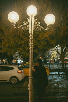 Woman smoking under a streetlight with cars passing by on a rainy urban night.