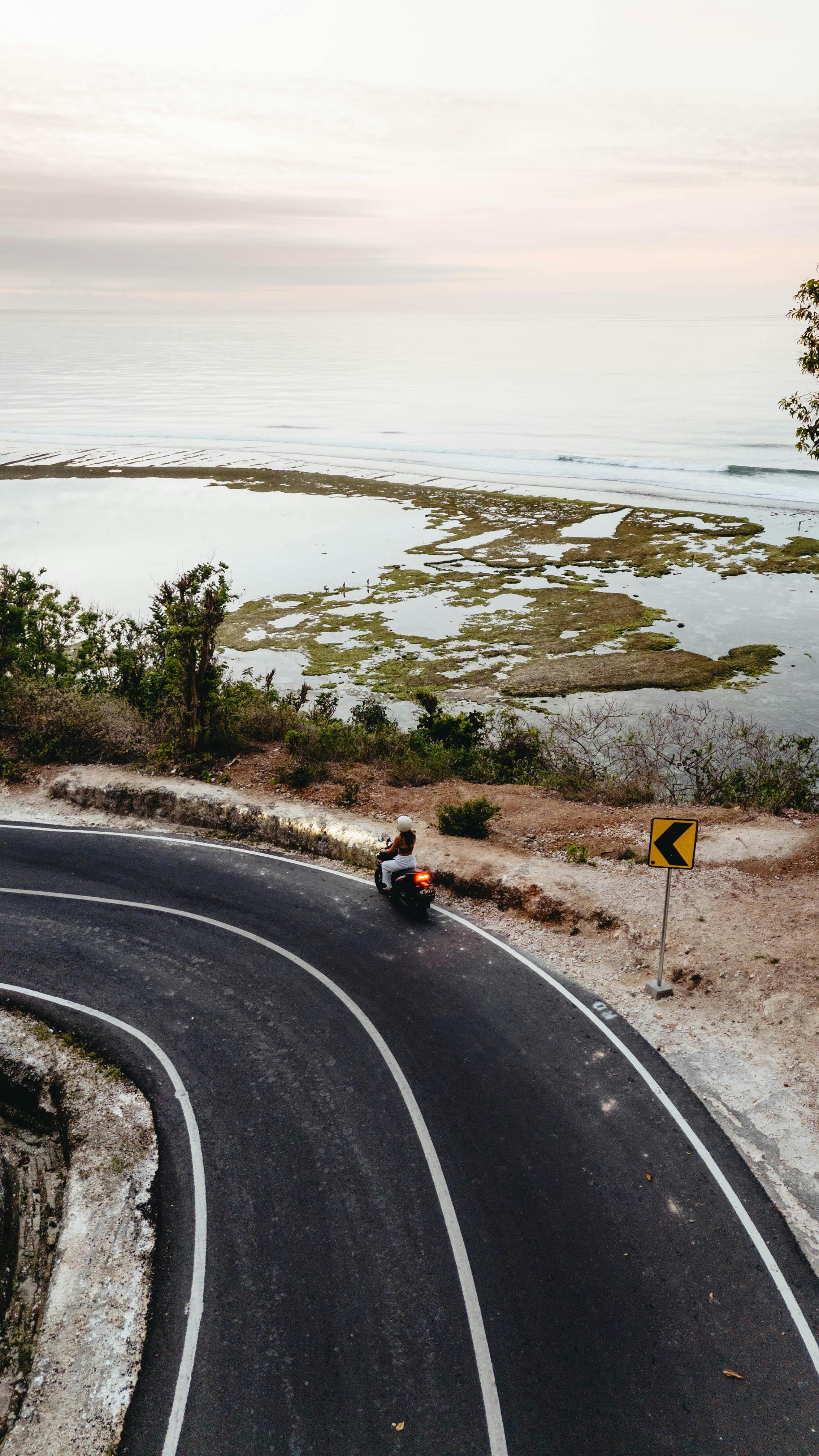Aerial view of motor scooter taking a curved coastal road with ocean background.