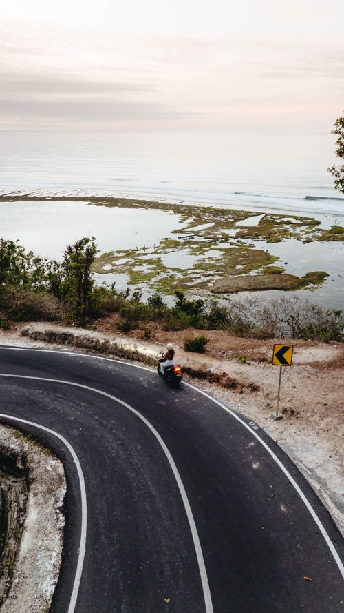 Free Aerial view of motor scooter taking a curved coastal road with ocean background. Stock Photo
