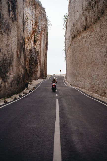 A solitary motorcyclist travels a narrow highway between towering rock formations.