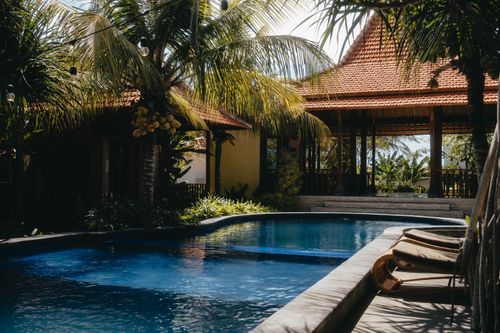 Free Relax by a luxurious tropical pool surrounded by lush palm trees under a sunny sky, perfect for summer getaways. Stock Photo