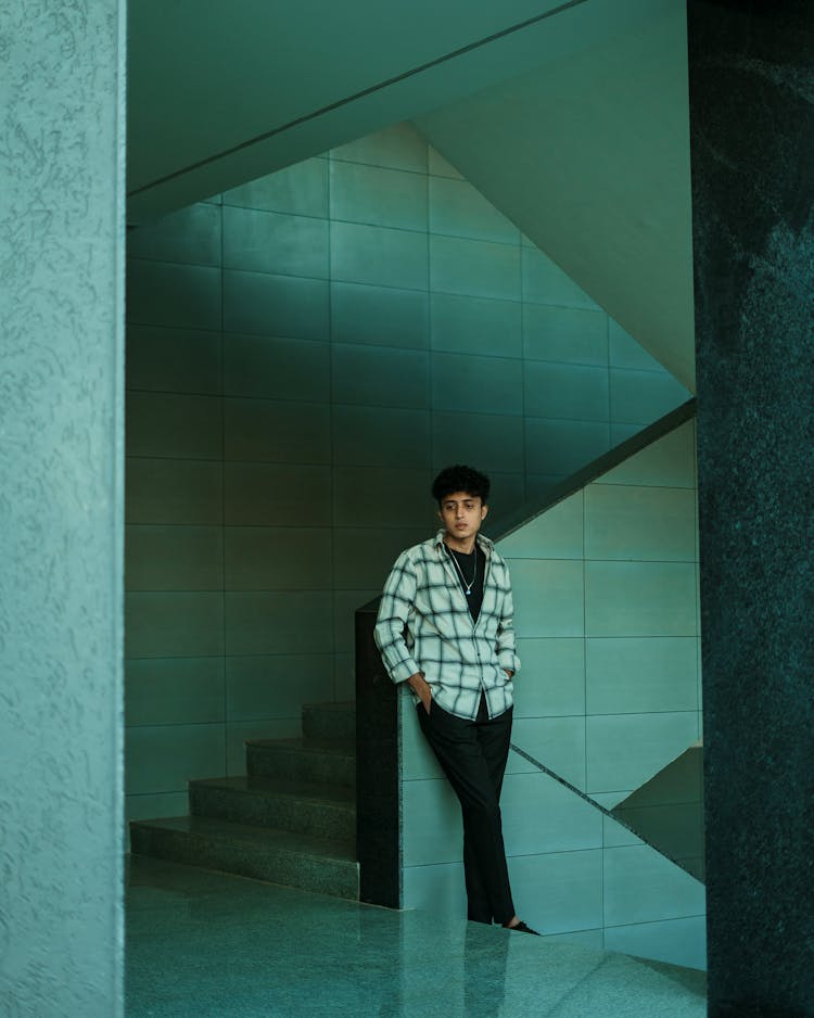 Man Wearing A Checked Shirt Leaning Against A Turquoise Staircase