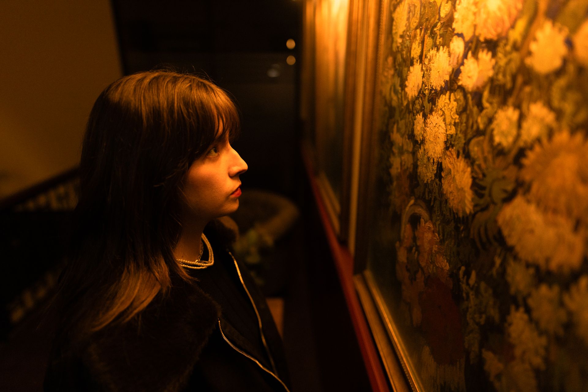 A young woman deeply engrossed in viewing paintings in a warmly lit art gallery.