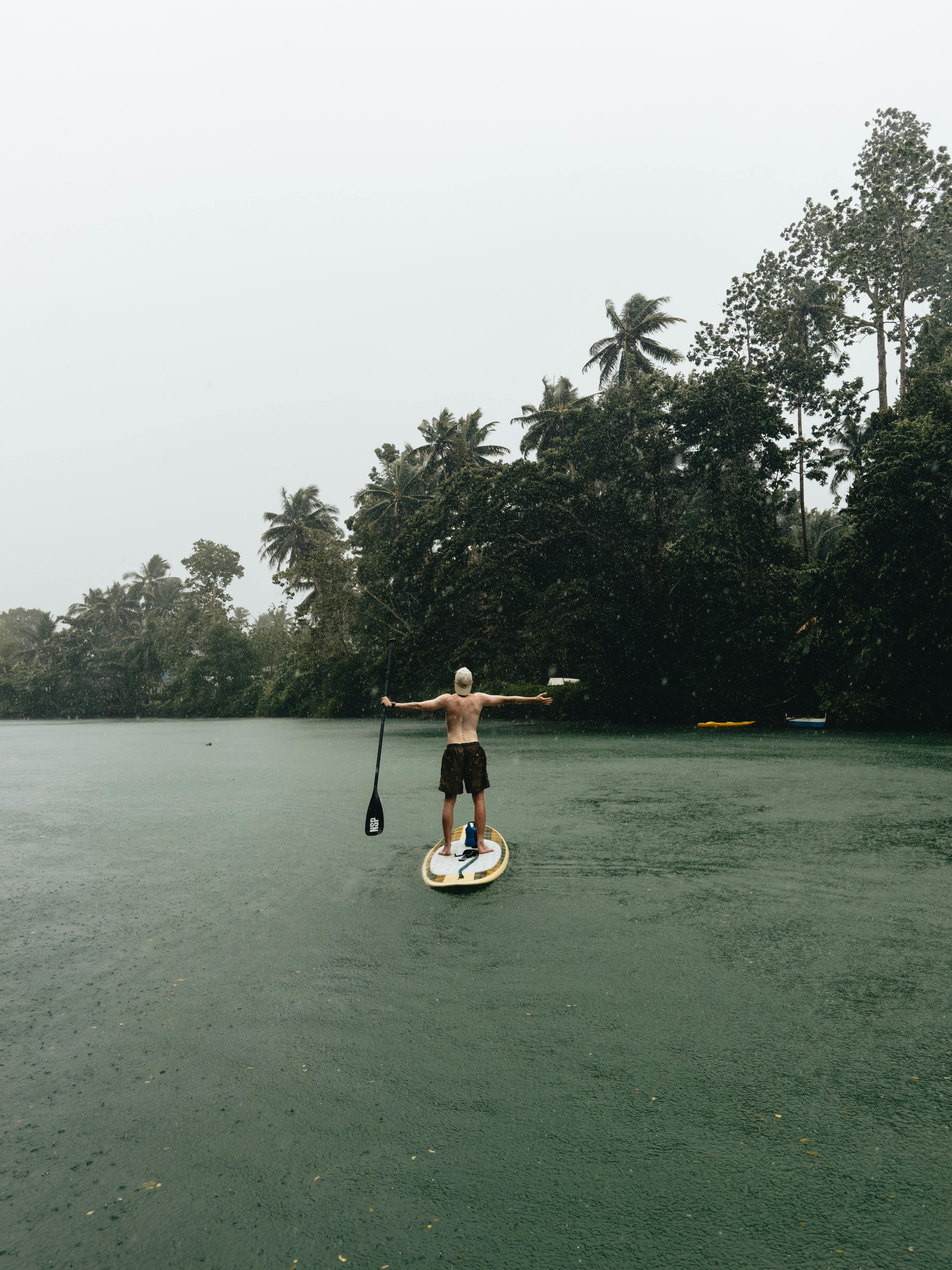 Shirtless man paddleboarding on a river surrounded by lush trees in Central Visayas, Philippines.