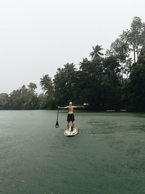 Shirtless man paddleboarding on a river surrounded by lush trees in Central Visayas, Philippines.