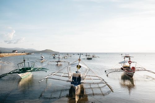 Free Peaceful scene of moored fishing boats at sunset along a serene coastal shore. Stock Photo
