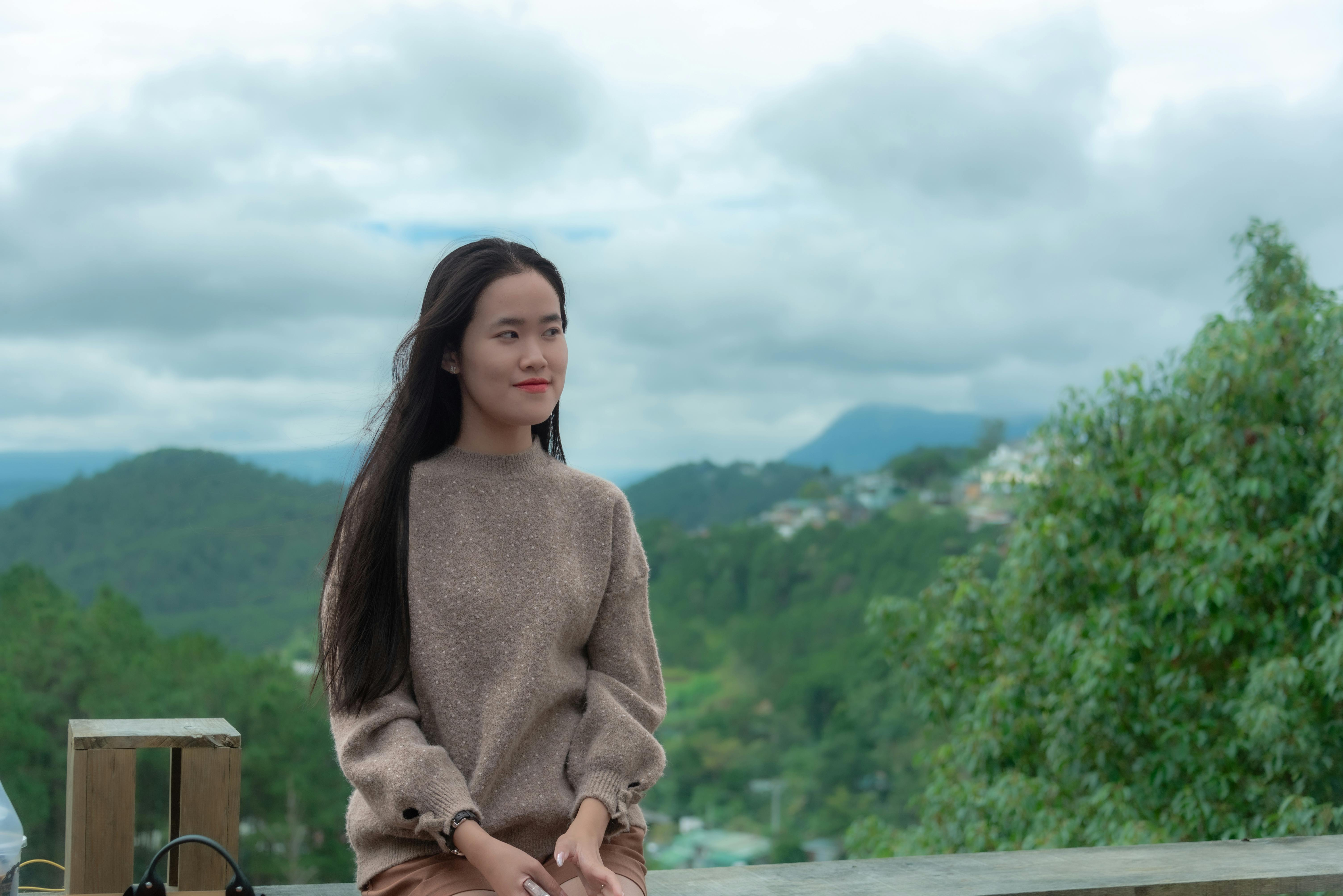 A young woman in a cozy sweater enjoying a scenic mountain view on a cloudy day.