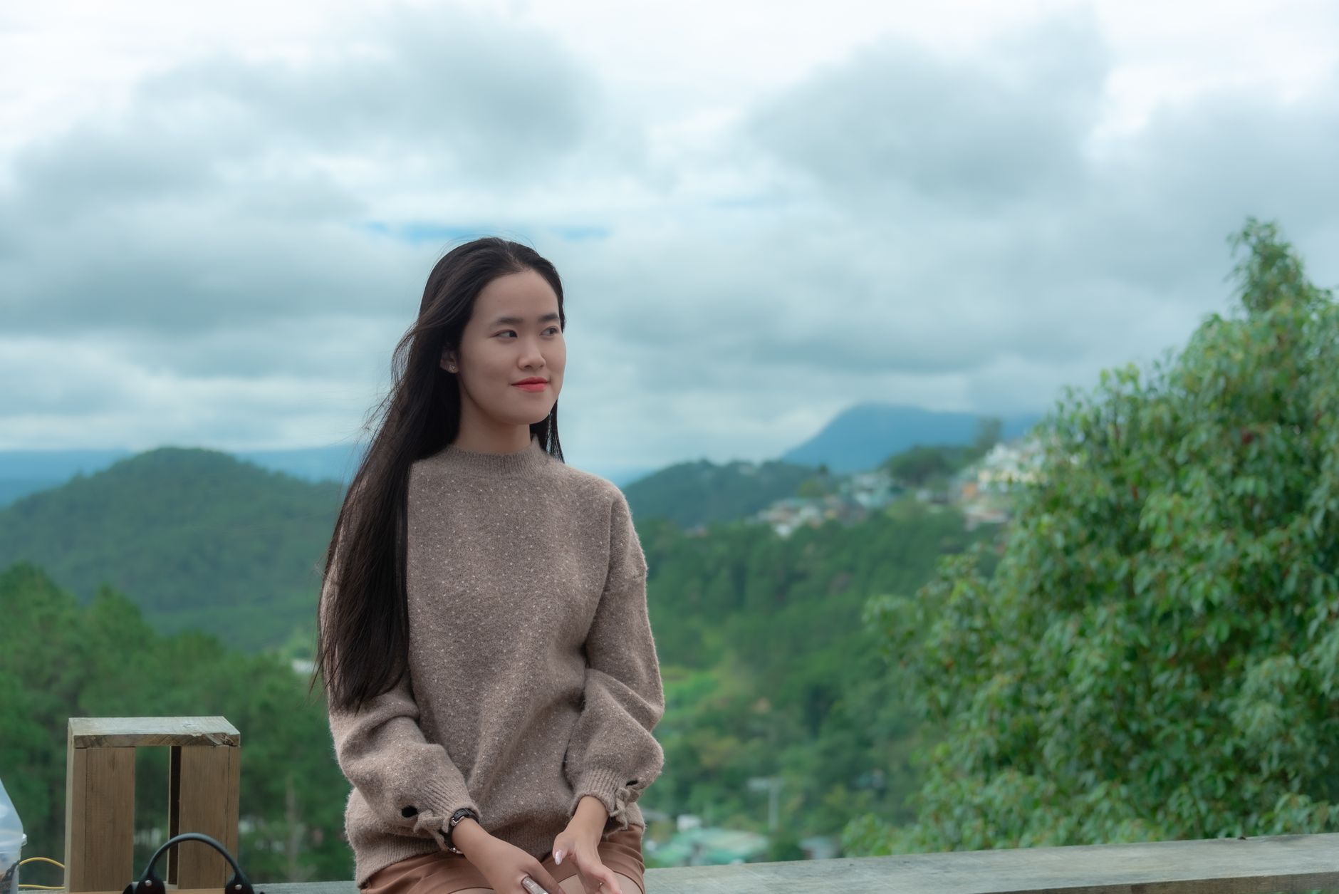 A young woman in a cozy sweater enjoying a scenic mountain view on a cloudy day.