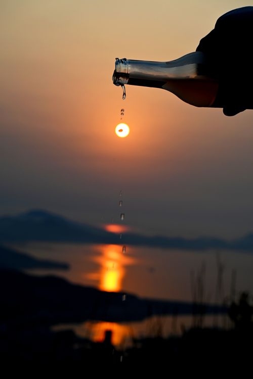 Free A scenic sunset view over the sea with a silhouette of a bottle pouring droplets, creating a serene coastal atmosphere. Stock Photo