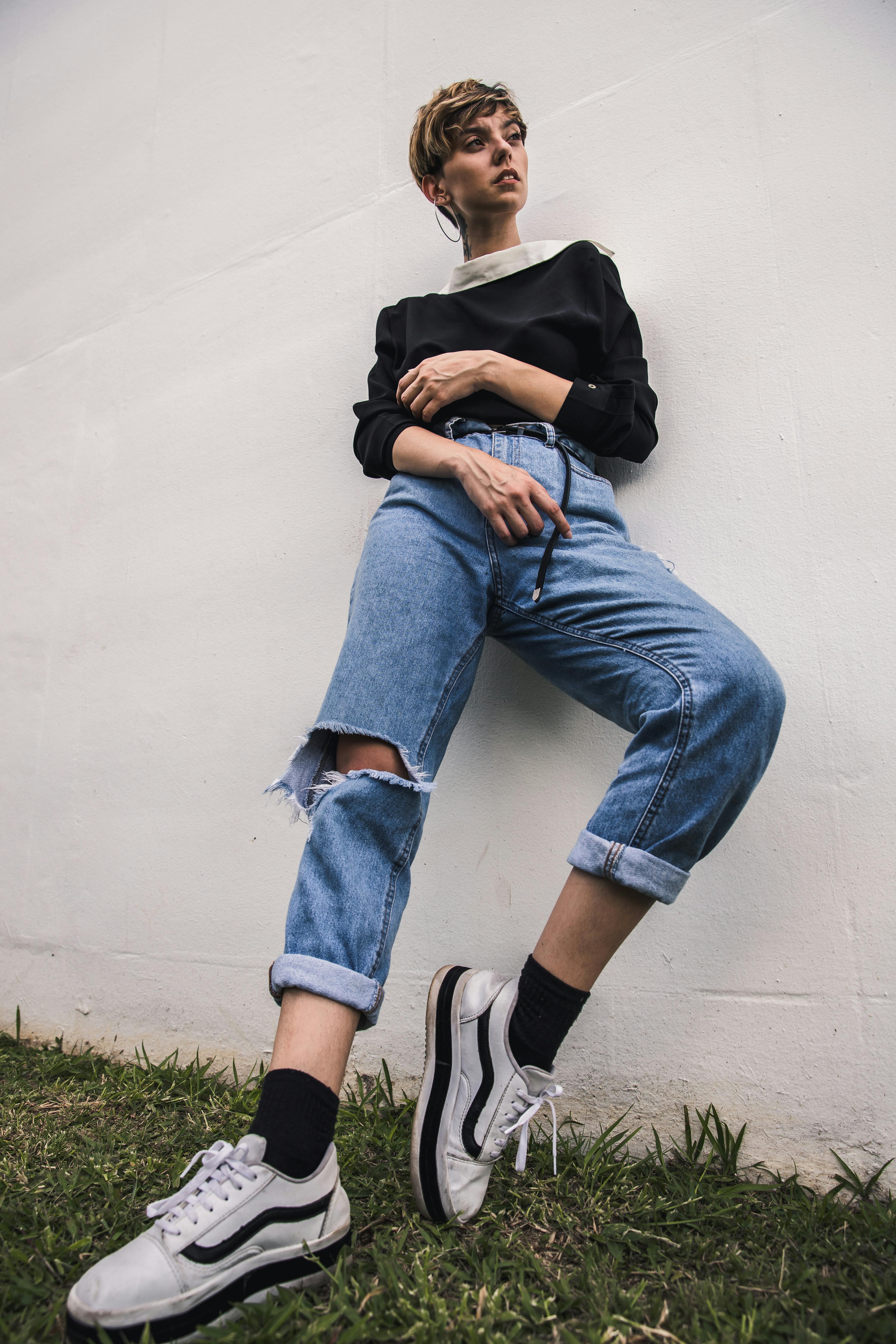 一位穿着破洞牛仔裤和运动鞋的时尚女性在户外斜身拍摄时尚照片