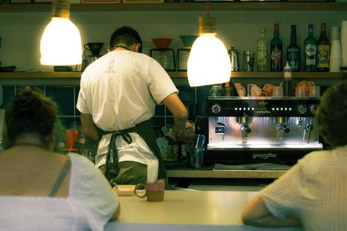 Free A barista skillfully prepares coffee at the espresso machine in a warmly lit café environment. Stock Photo