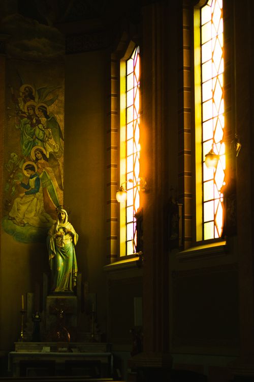 Free Beautiful church interior featuring stained glass windows and religious statue bathed in warm sunlight. Stock Photo