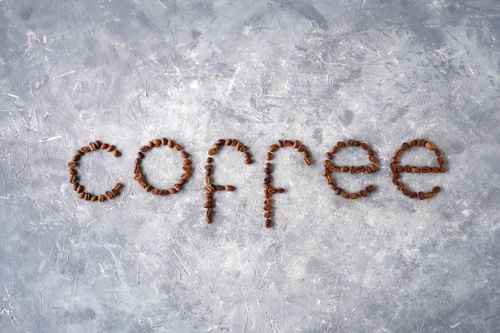 Free Creative arrangement of coffee beans spelling 'coffee' on a textured gray surface. Stock Photo