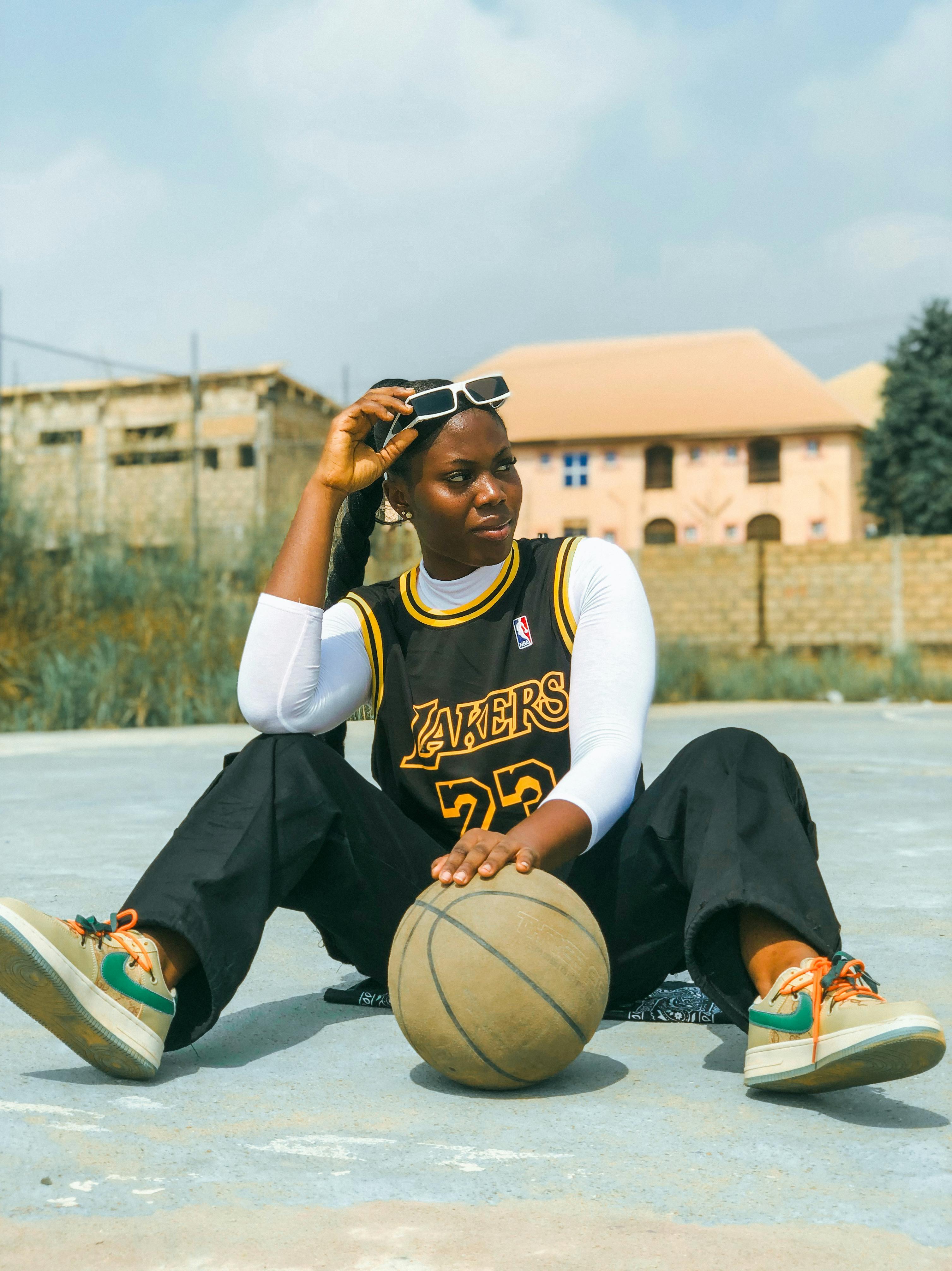 young woman in los angeles lakers jersey sitting on basketball court with a ball