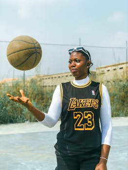 Athletic woman spinning a basketball outdoors in Lakers jersey on a sunny day.