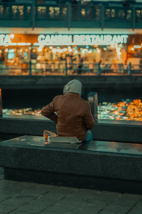 Man Sitting on a Bench in a City at Dusk