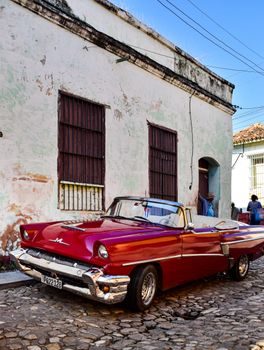 A classic red convertible parked on a cobbled street in a historic Cuban town.