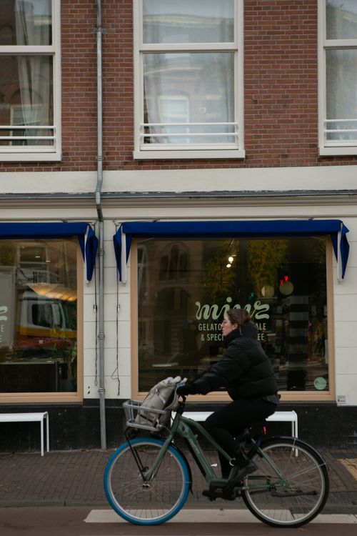 Free Bicyclist passes by a cafe on a city street, highlighting urban lifestyle. Stock Photo