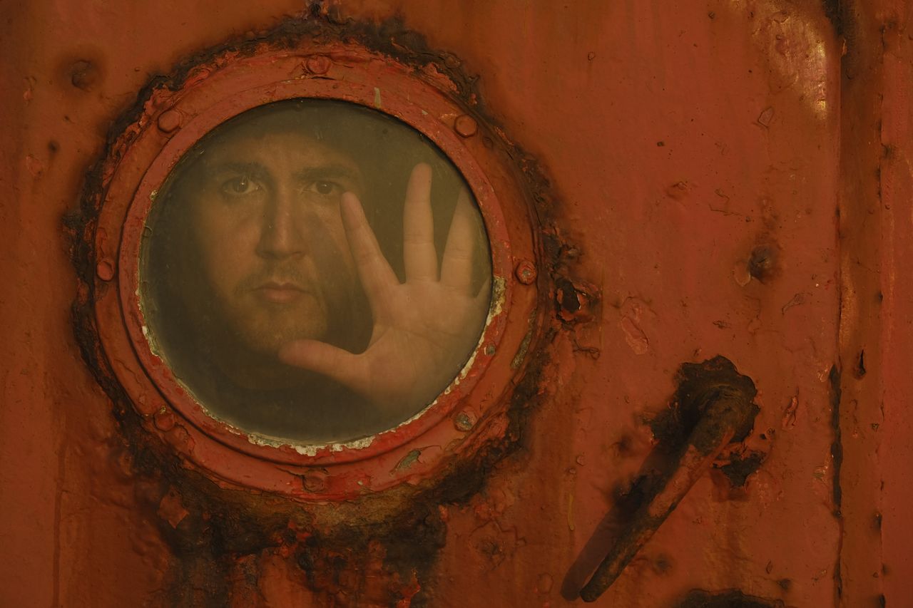 a man peers through a round rusty porthole window creating a mysteriou