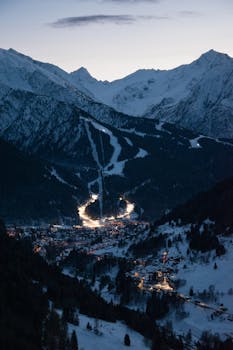 Charming evening aerial view of snowcapped Ponte di Legno in Lombardy, Italy, nestled between illuminated mountains.
