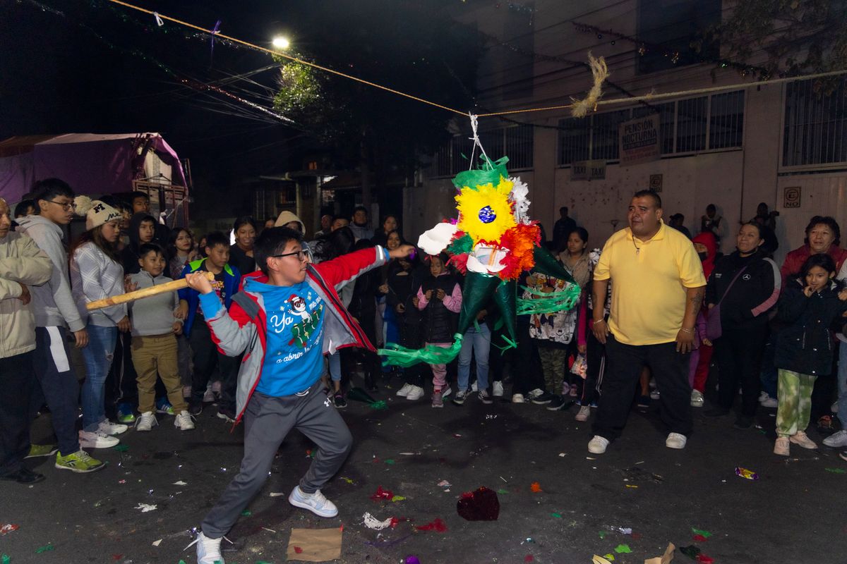 Lively night street scene in Coyoacán, CDMX, with children breaking a colorful piñata.