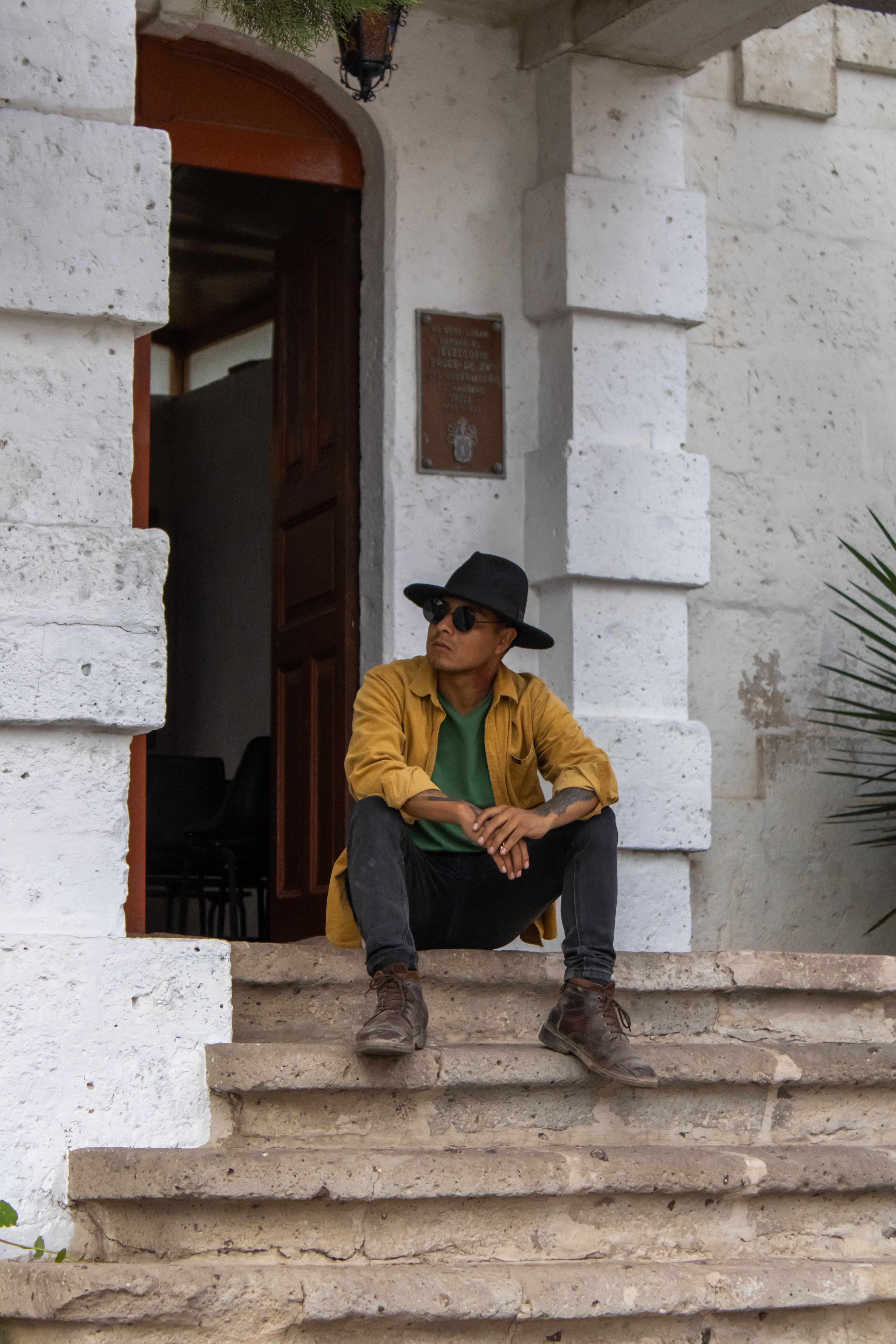 Man with hat and sunglasses sitting on steps, city urban vibe in Cayma, Arequipa, Peru.