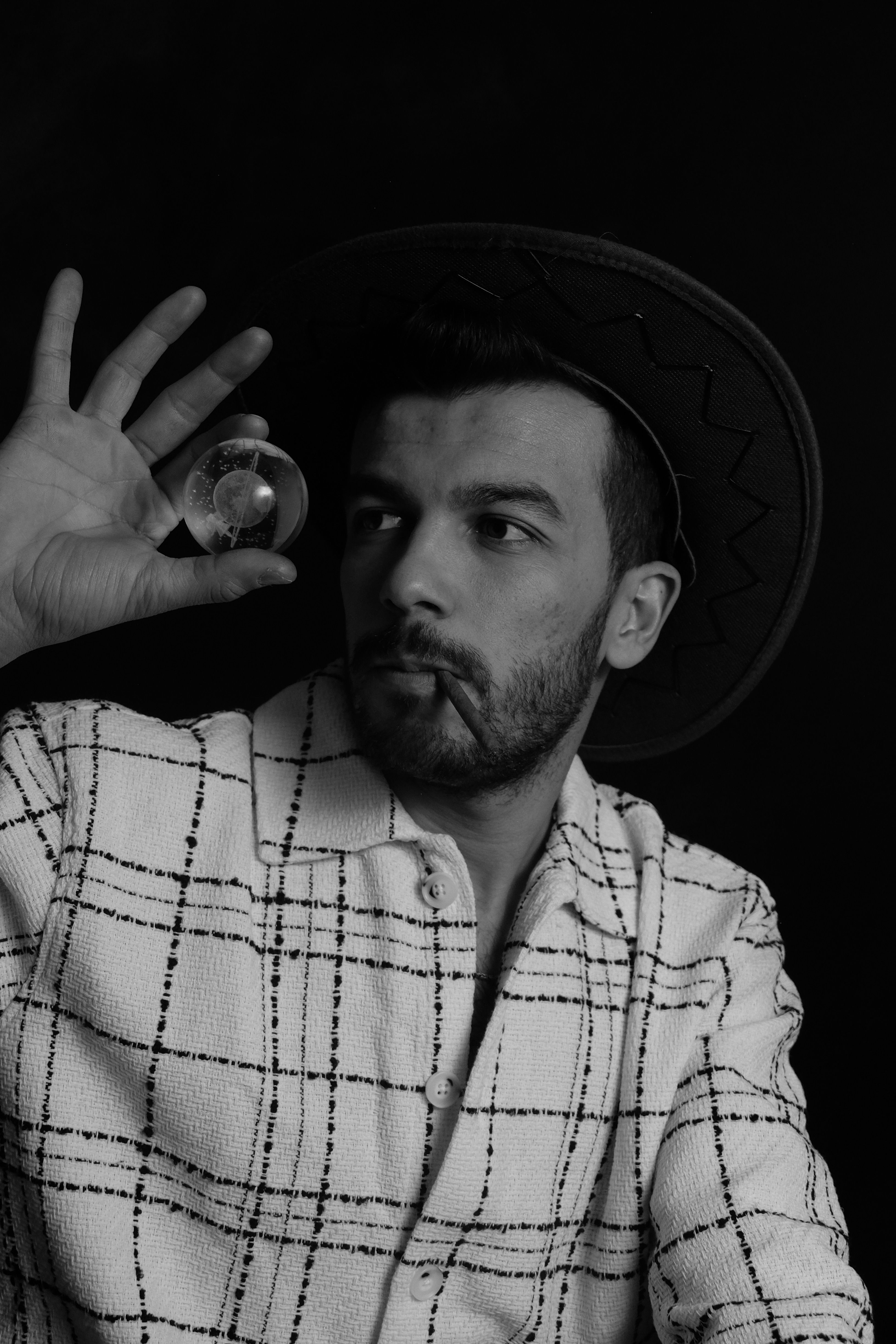 Black and white portrait of a man wearing a cowboy hat, holding a ball against a dark background.