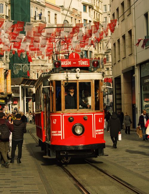 Free Iconic red tram moving down bustling Istanbul street in daylight with flags and pedestrians. Stock Photo