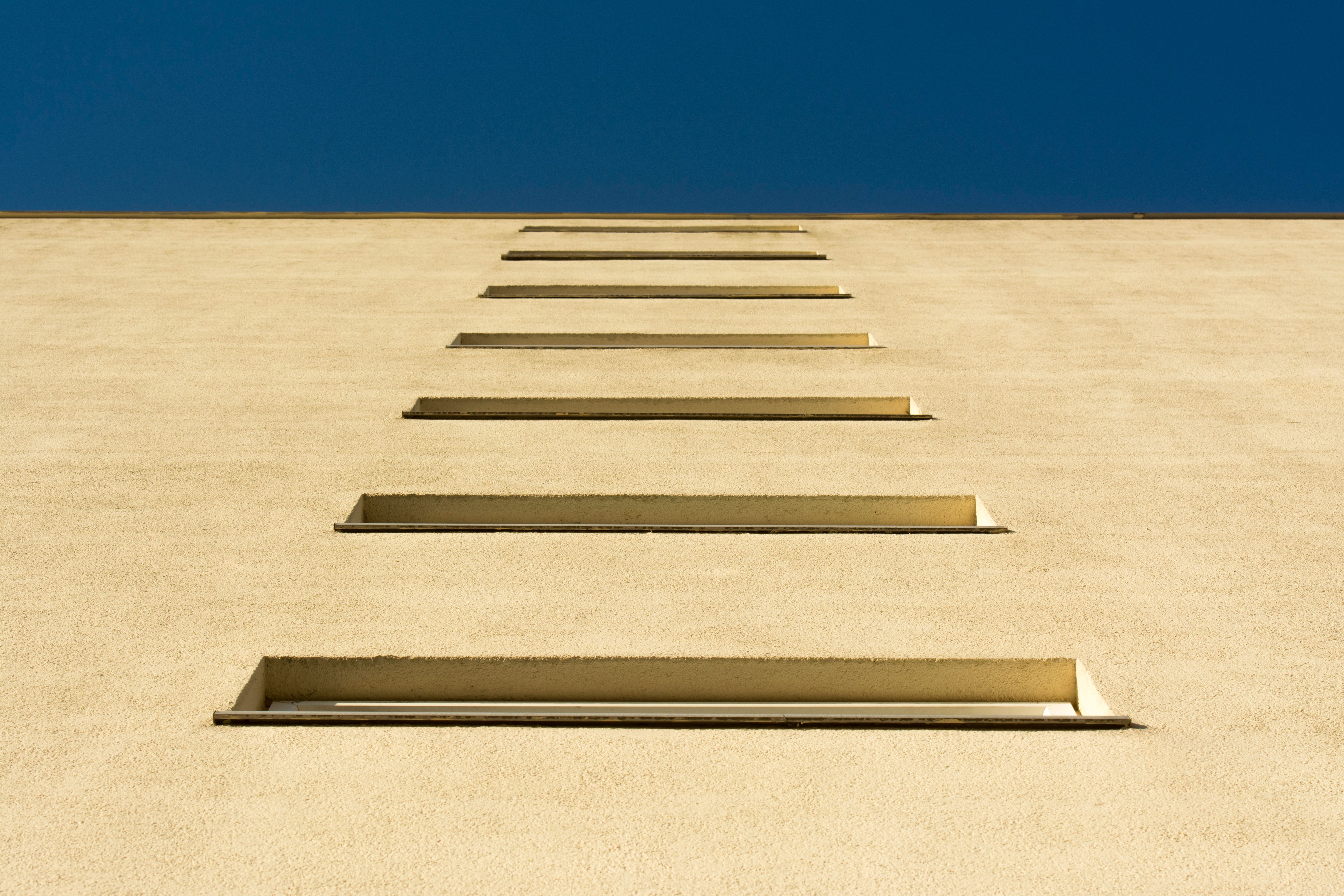 Low angle view of a symmetrical building facade with a clear blue sky, showcases repeating window pattern.