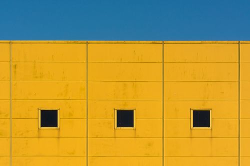 Free Simple urban architecture with three windows on a bright yellow wall under a clear blue sky. Stock Photo