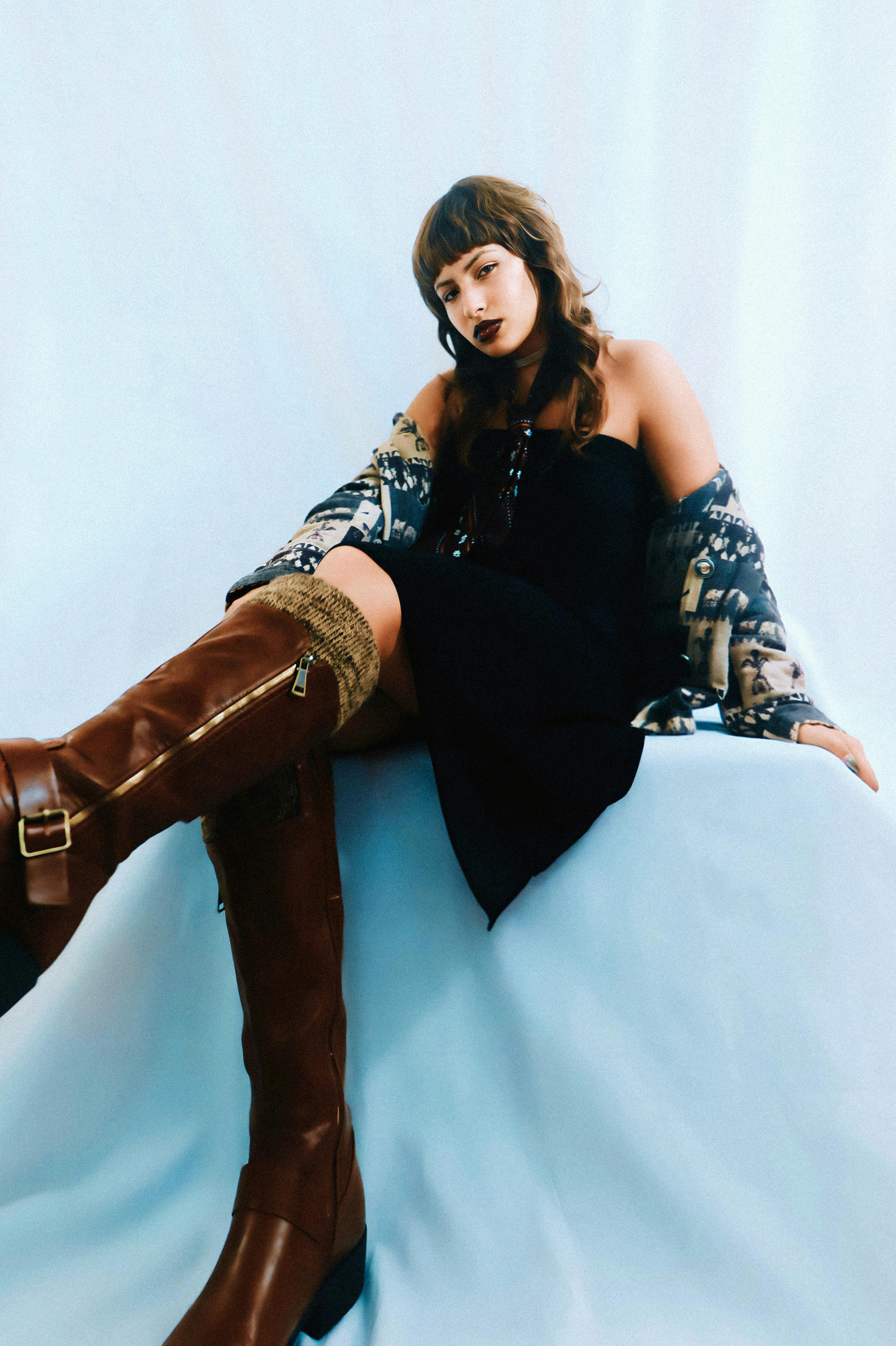 Portrait of a stylish young woman in modern boots, sitting confidently in a studio setting.