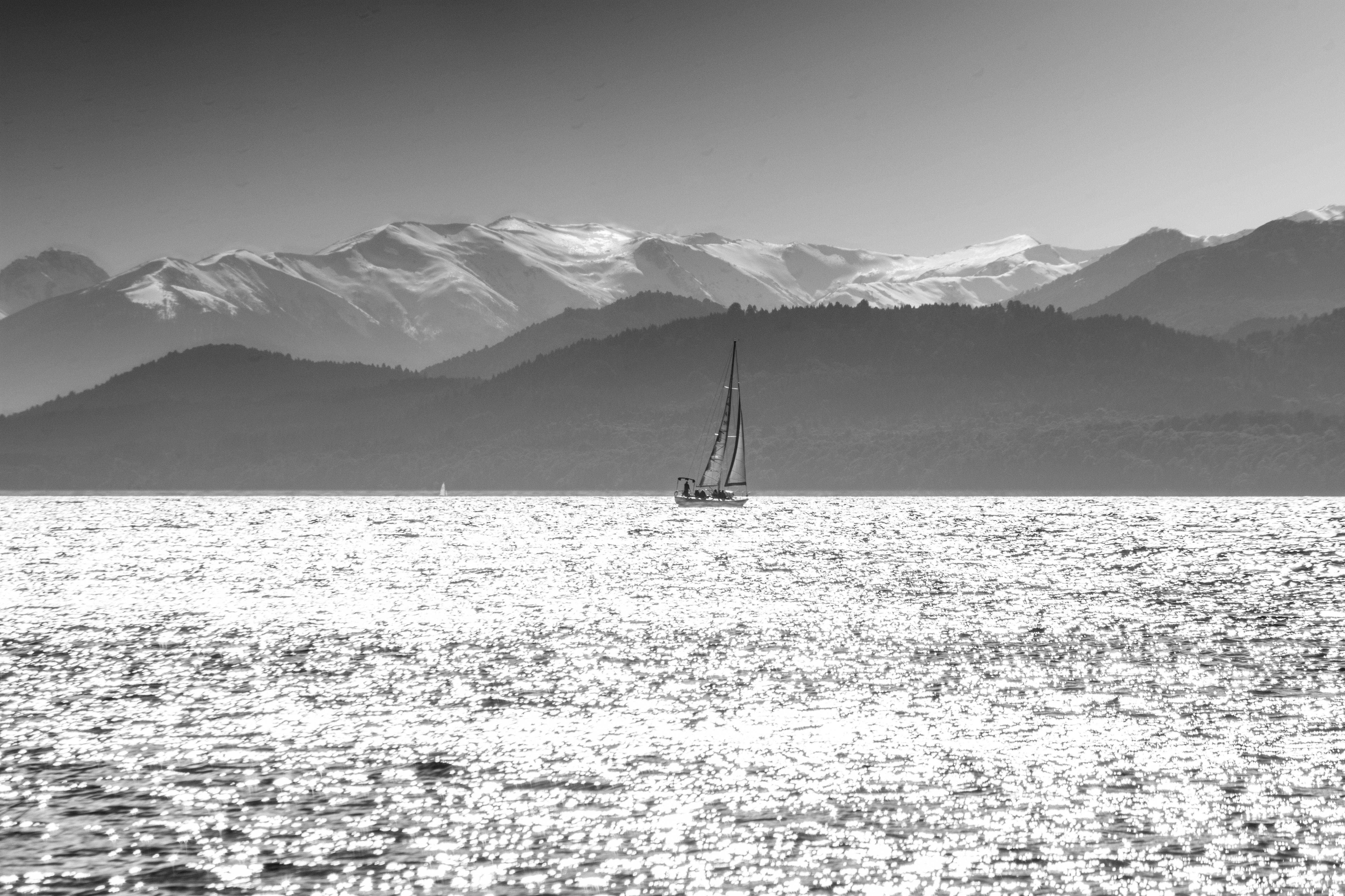 Stunning black and white image of a sailboat on Lake Nahuel Huapi, framed by the Andes Mountains in San Carlos de Bariloche, Argentina.