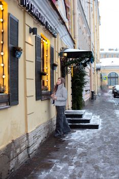 Woman in winter attire standing outside a Georgian restaurant on a snowy city street.