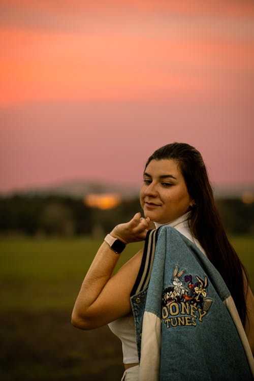 Young Woman Standing on a Meadow at Sunset 