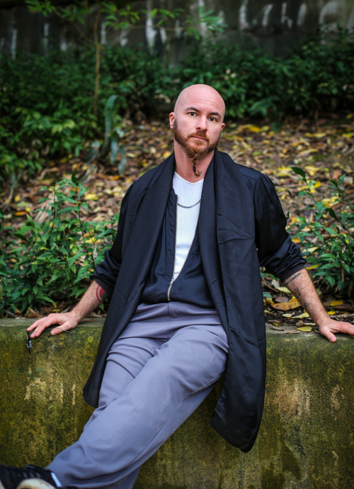 Free Bald man with a beard relaxing in an outdoor park setting, wearing casual attire. Stock Photo
