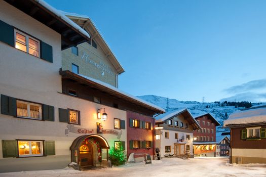 A picturesque street with snow-covered Alpine architecture in evening light.
