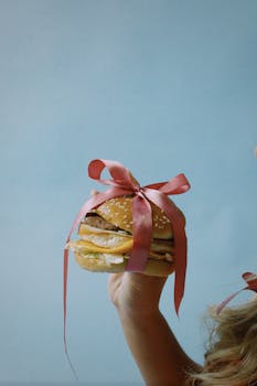Burger with pink ribbon held by child for playful celebration theme.
