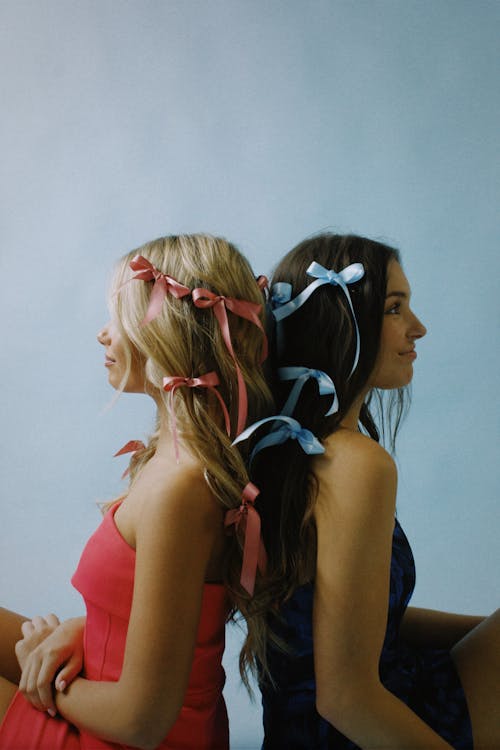 Young Women with Ribbons in Hair Sitting Back to Back 