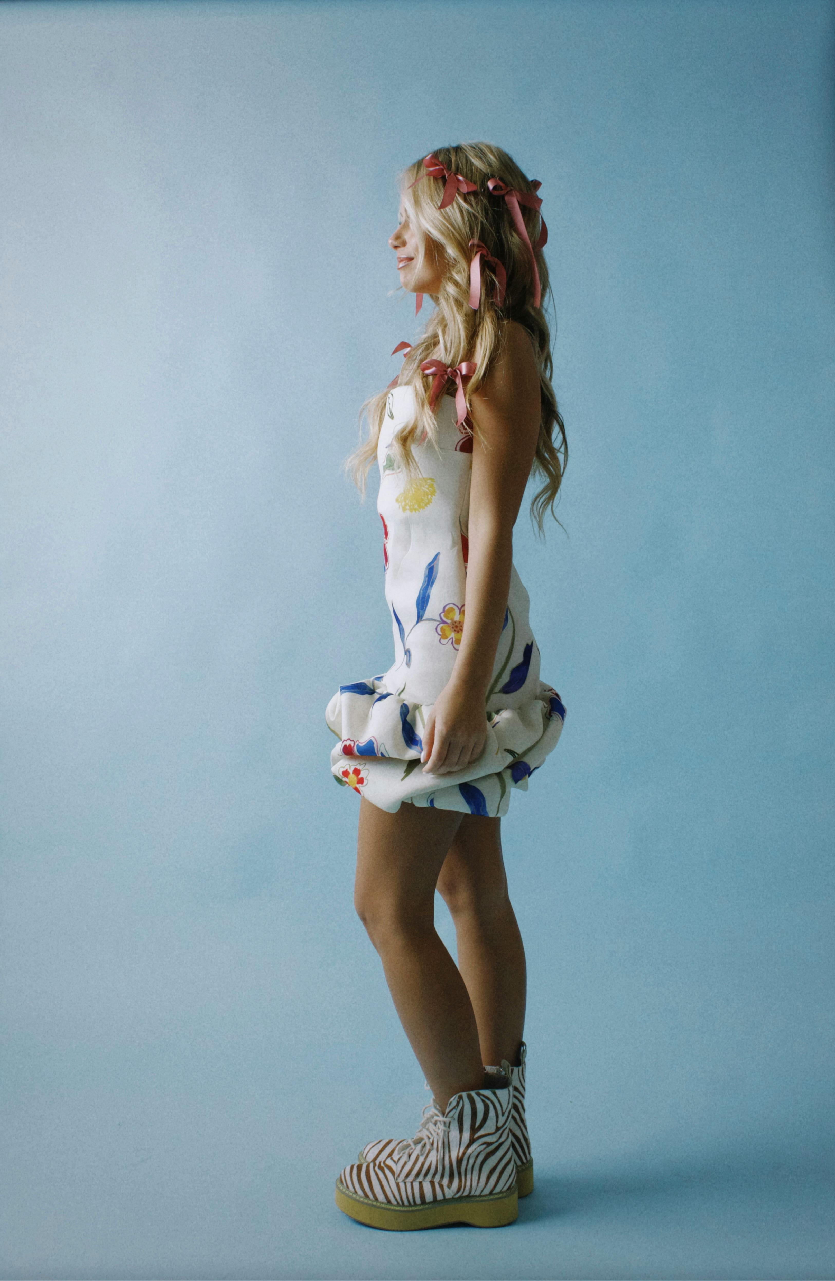 Fashionable young woman in a floral dress with ribbon accessories, posing against a blue background.