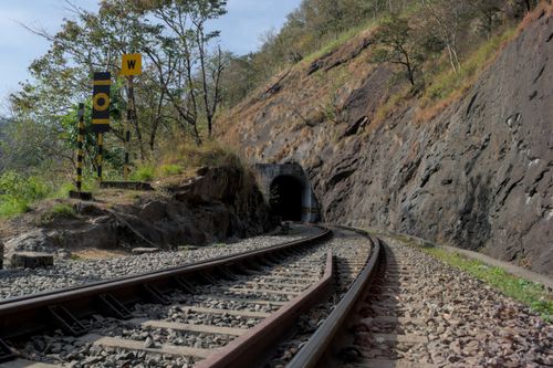 Free Railway tracks leading to a tunnel through a rocky hill, surrounded by trees and nature. Stock Photo