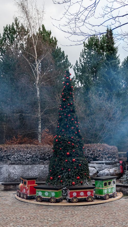 Free A beautiful Christmas tree adorned with ornaments and a toy train, set in a winter park. Stock Photo
